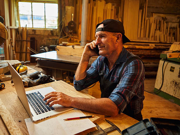 Tradesman at workbench using computer and phone to grow business with content marketing services.