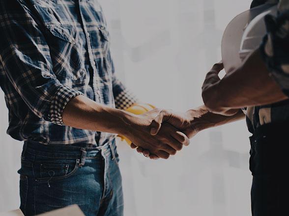 Home service contractor in plaid shirt shaking hands with client at job site.